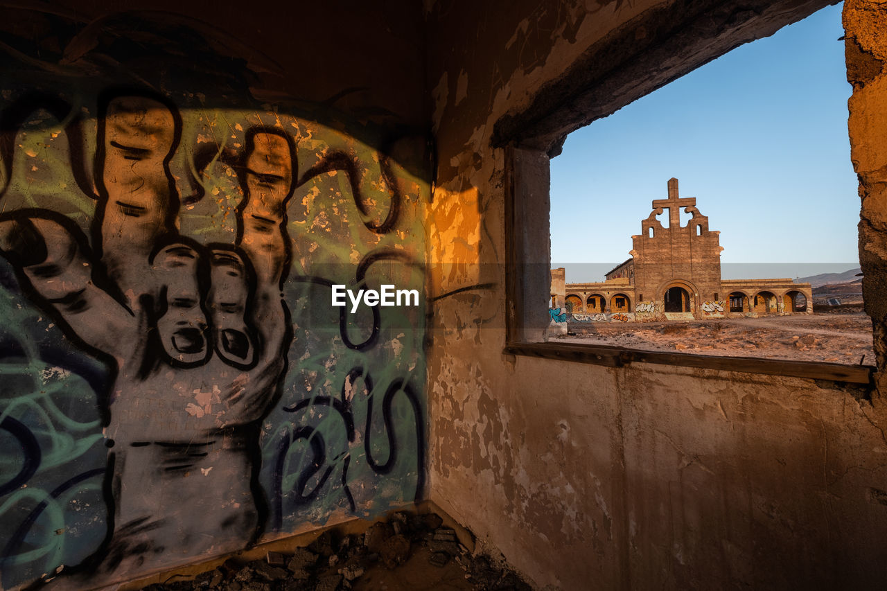 Abandoned abades church seen through windows of old houses at sunrise.