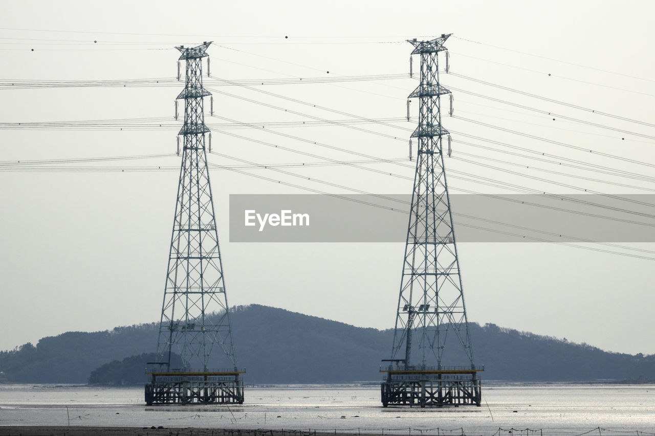 Electricity pylons at beach against clear sky