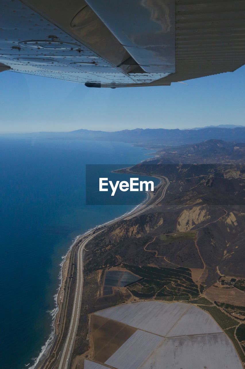 Cropped image of airplane flying over landscape by sea