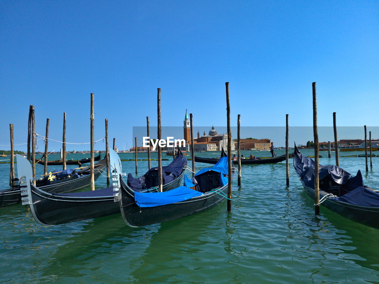 nautical vessel, water, gondola, transportation, mode of transportation, boat, vehicle, travel destinations, travel, nature, sea, moored, sky, watercraft, clear sky, canal, architecture, wooden post, boating, no people, tourism, blue, mooring post, wood, lagoon, outdoors, post, day, pole, scenics - nature, building exterior, built structure, waterfront, in a row, beauty in nature, tranquility, long-tail boat