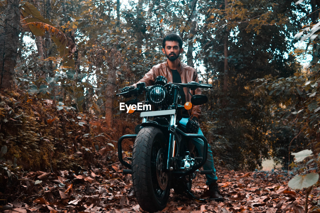 Portrait of man with umbrella on leaves in forest