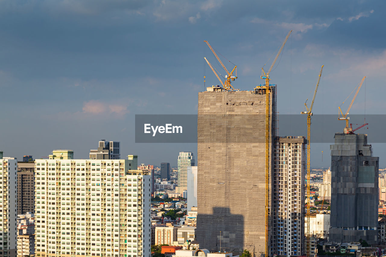 High rise building under construction, construction crane and modern city.