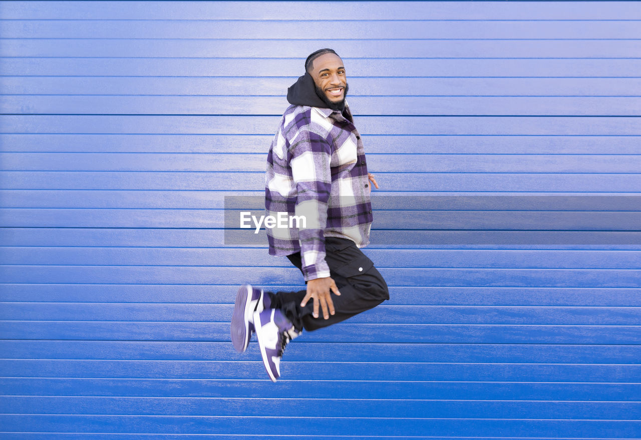 Happy young man in mid-air against blue corrugated iron