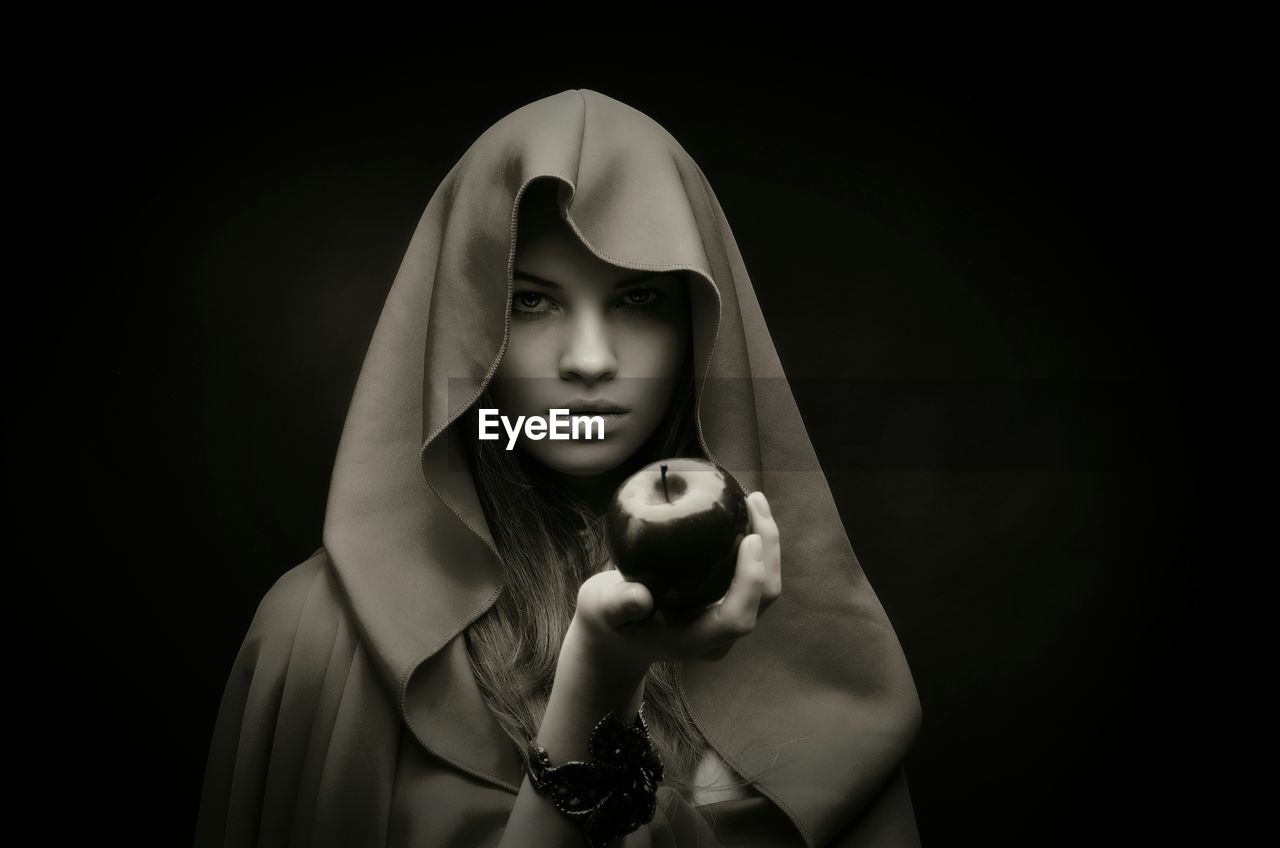 Portrait of woman holding apple in traditional clothing against black background