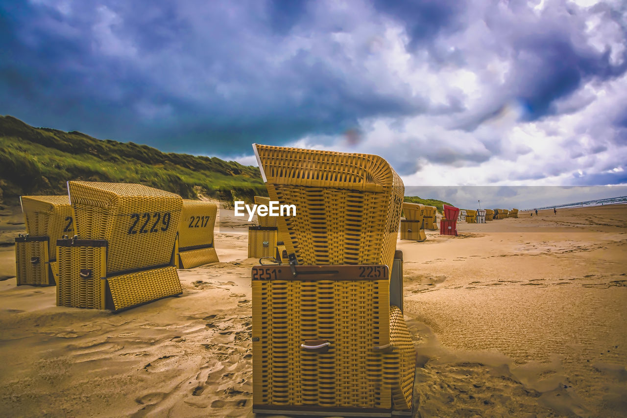 Hooded beach chairs on sand against sky