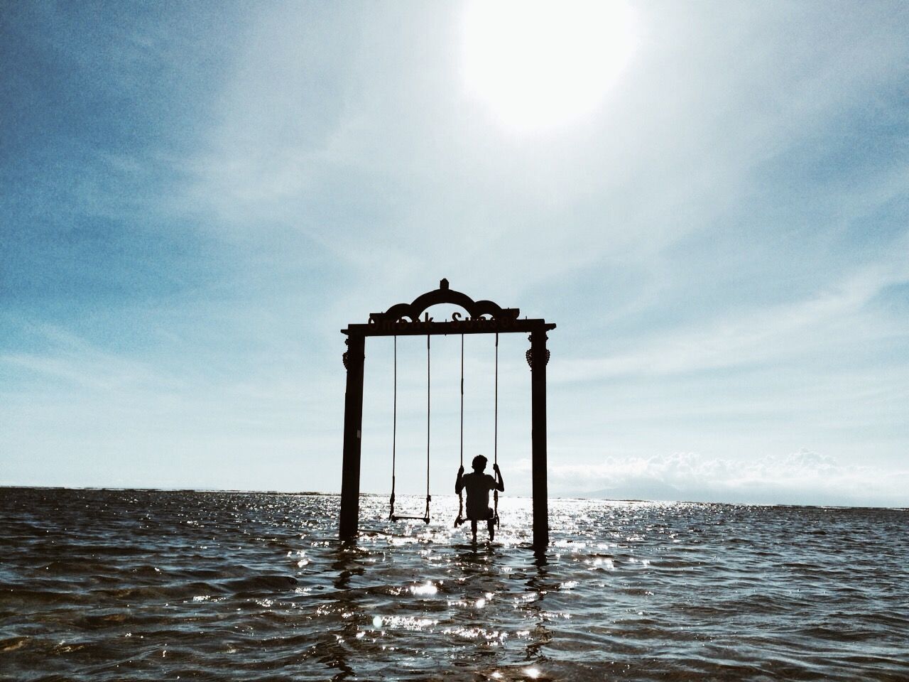 Silhouette person on swing amidst sea against sky