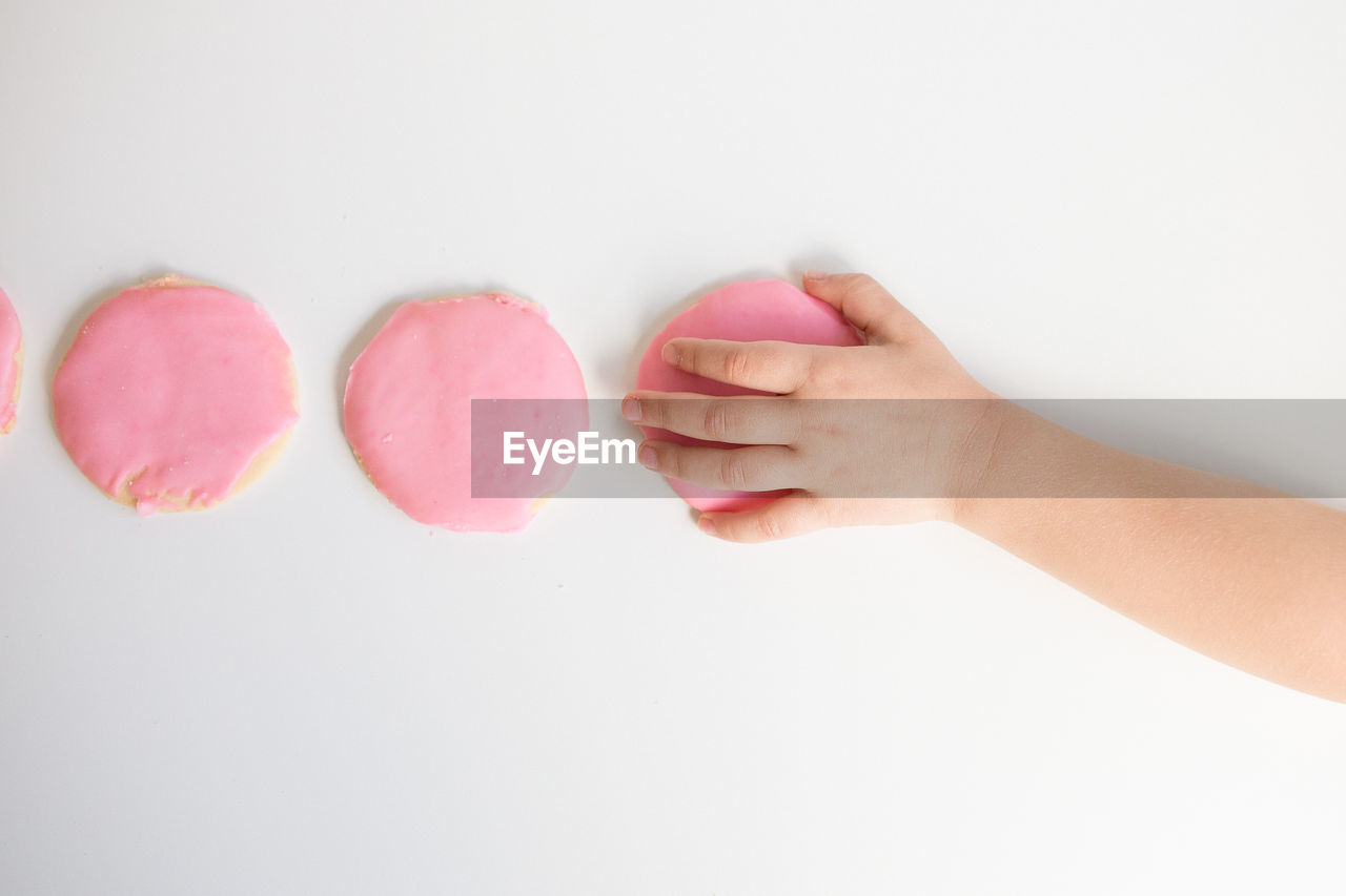 Overhead view of child's hand taking pink frosted sugar cookie
