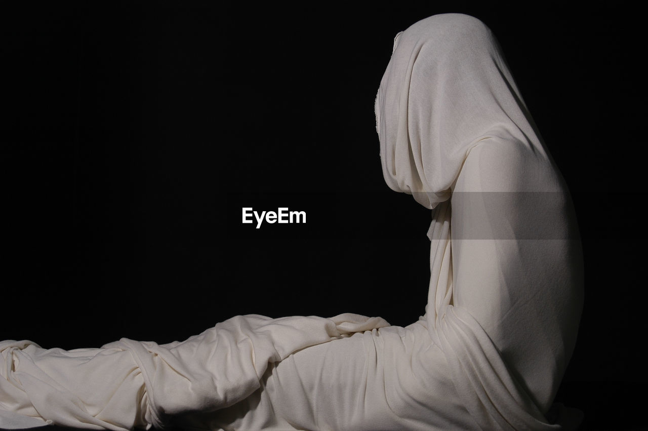 Person wrapped in white fabric against black background