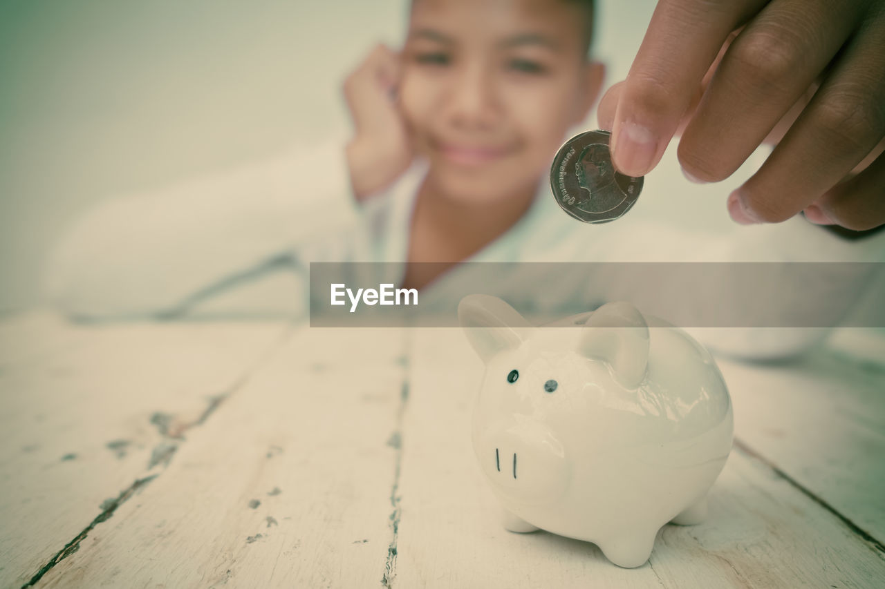 Portrait smiling boy putting coin in piggy bank on table at home