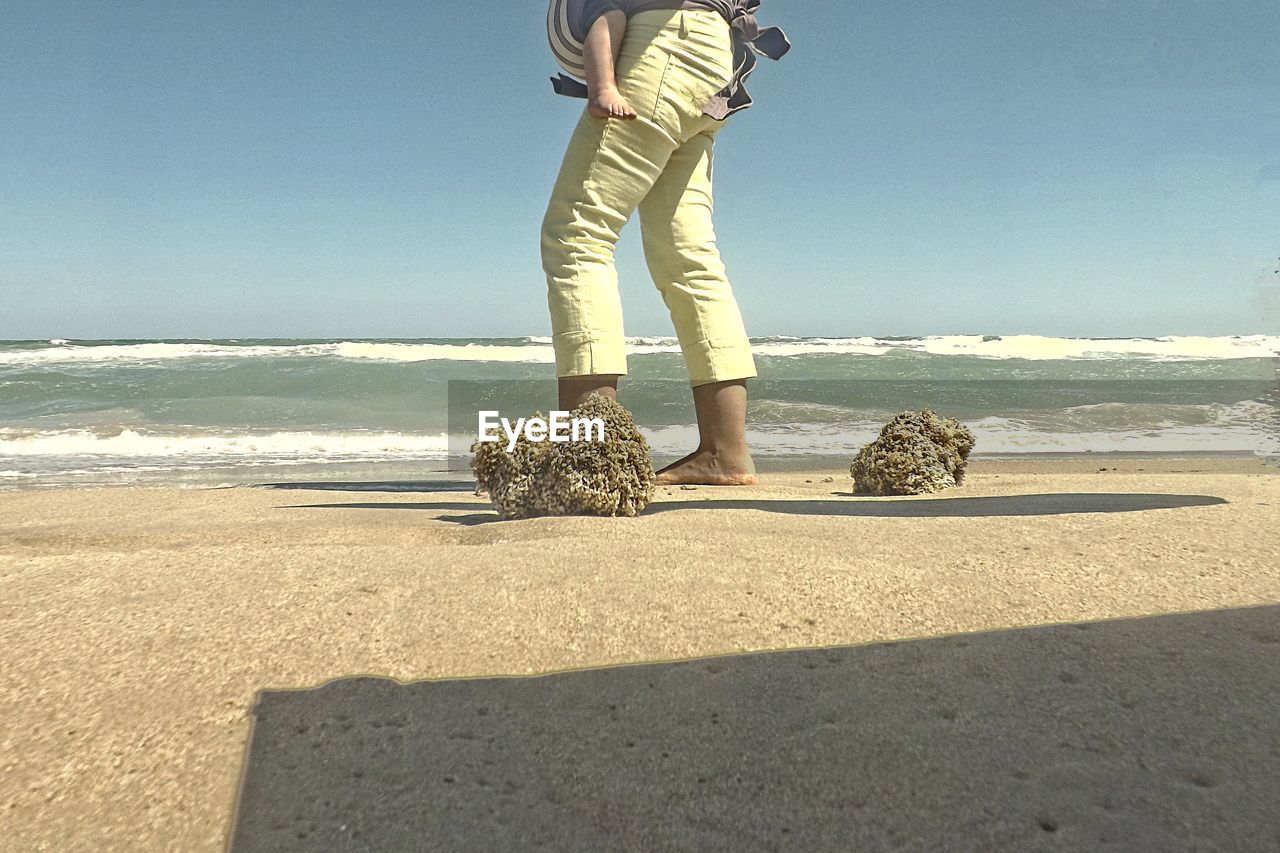 Low section of woman carrying baby at beach against sky