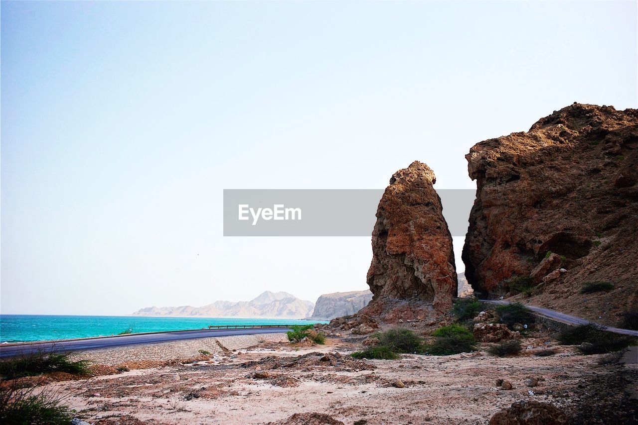 Scenic view of cliff by sea against clear sky