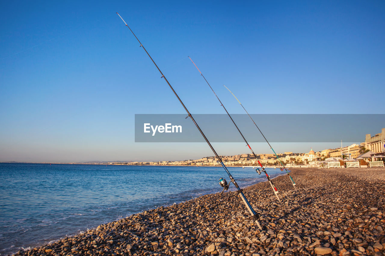 Fishing rods on a pebble beach on promenade des anglais at dawn, nice, france
