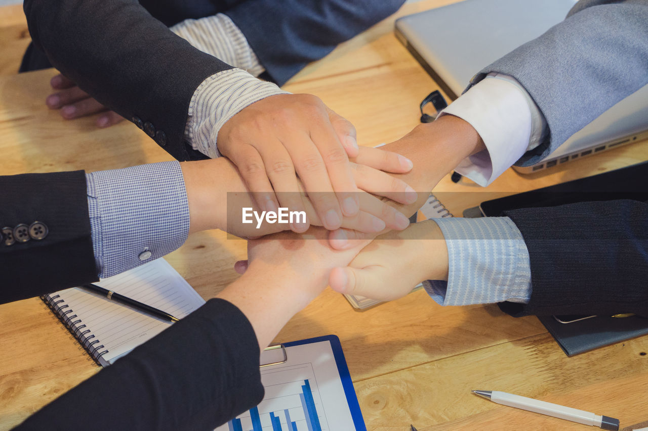Cropped hands of business coworkers stacking hands at desk in office
