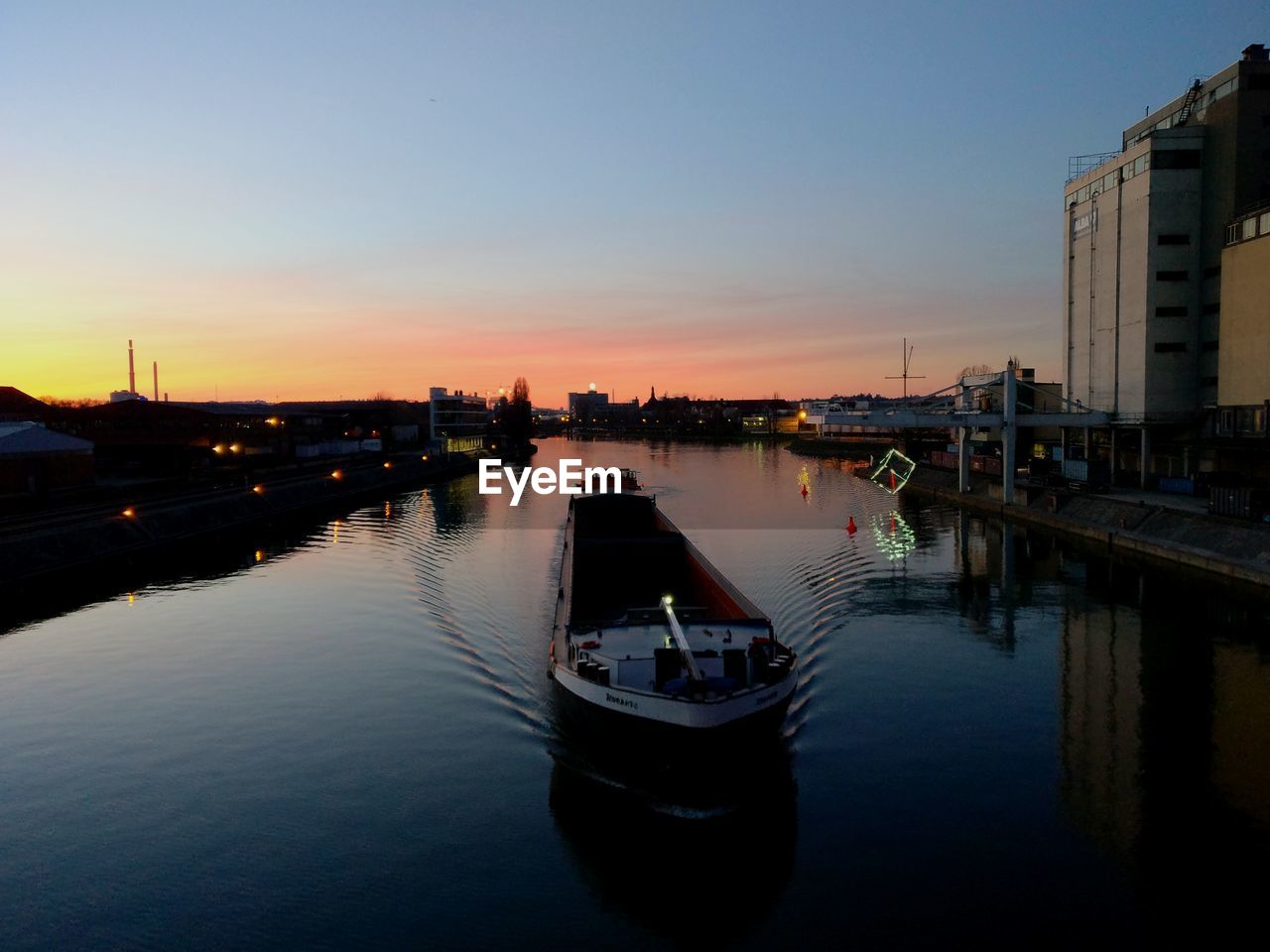 High angle view of barge sailing on river in city against sky during sunset