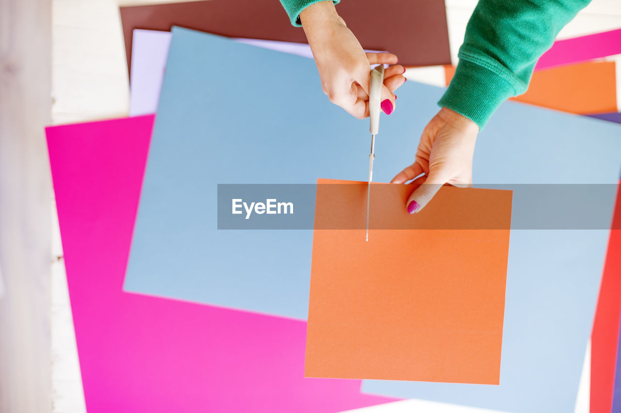 Cropped hands of woman cutting orange kraft paper on table