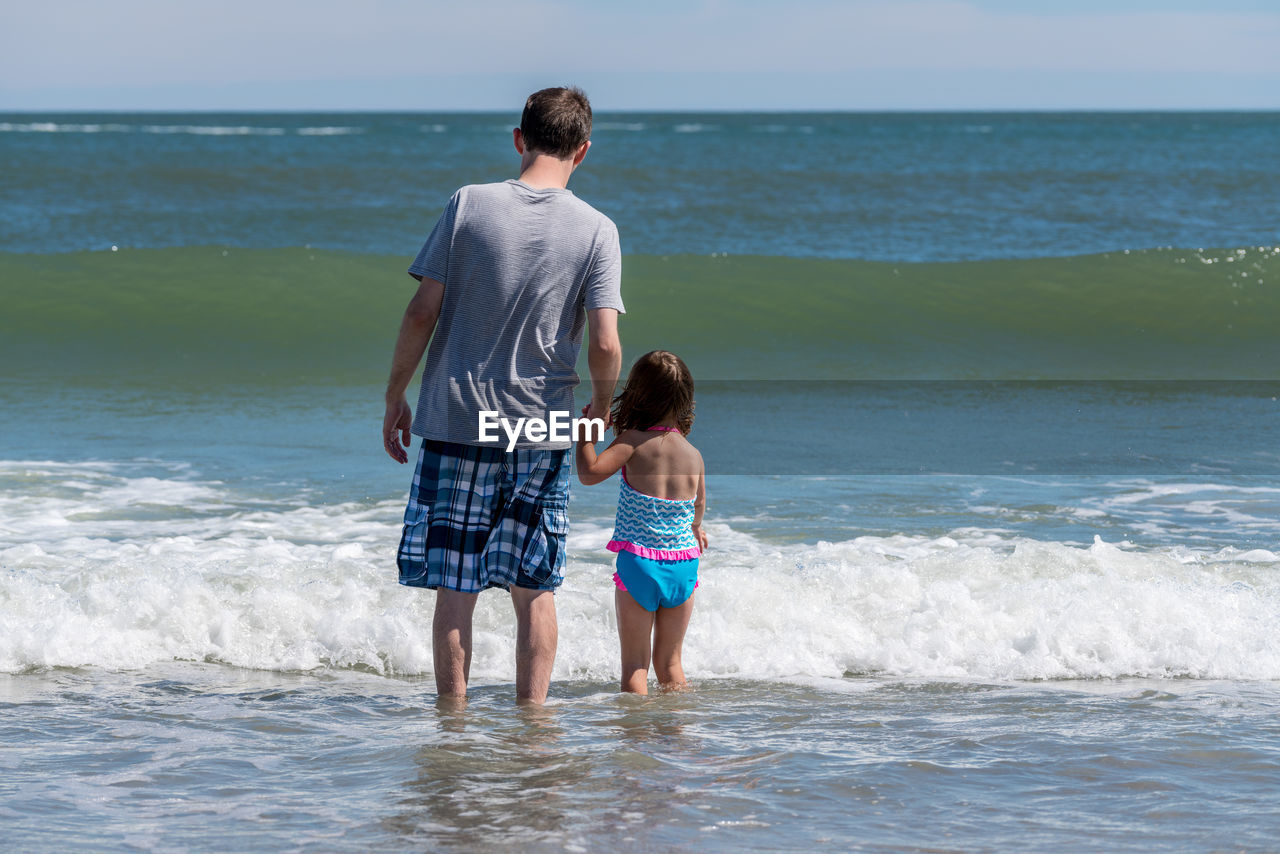 REAR VIEW OF MEN STANDING ON BEACH