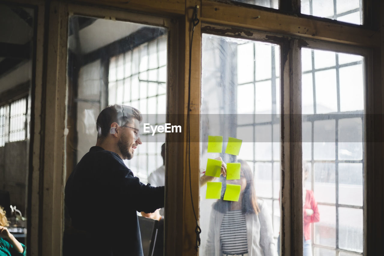 Businessman writing on adhesive note while having meeting with female programmer at creative office