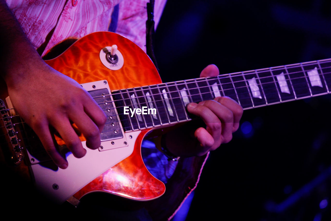 Midsection of man playing guitar at concert