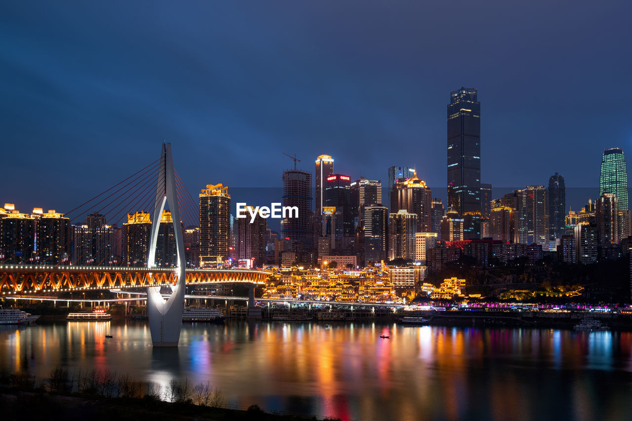 ILLUMINATED BUILDINGS BY RIVER AGAINST SKY