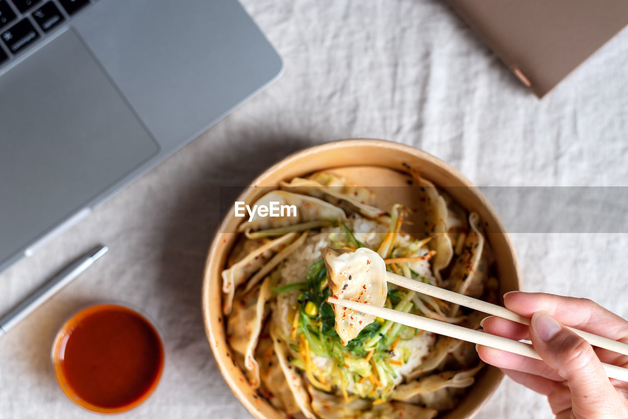 Asian takeaway food box with rice and dumplings on the office desk near the laptop.