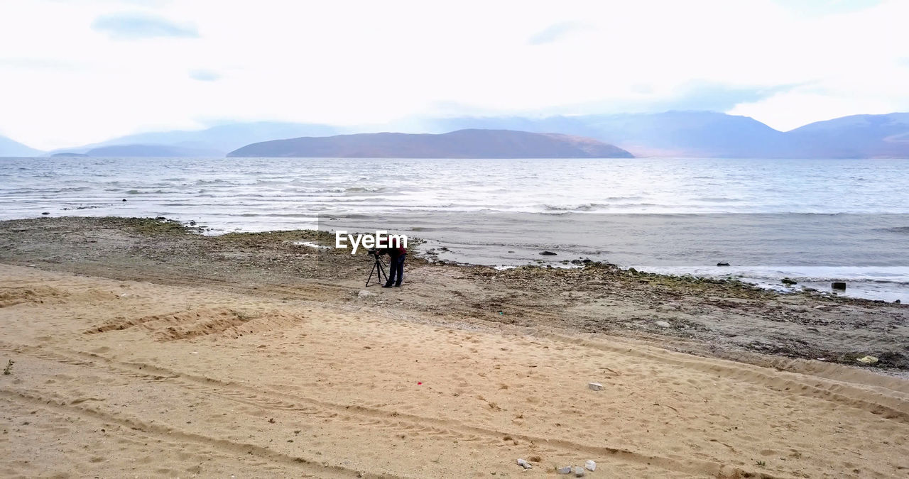 Man with tripod standing against sea at beach