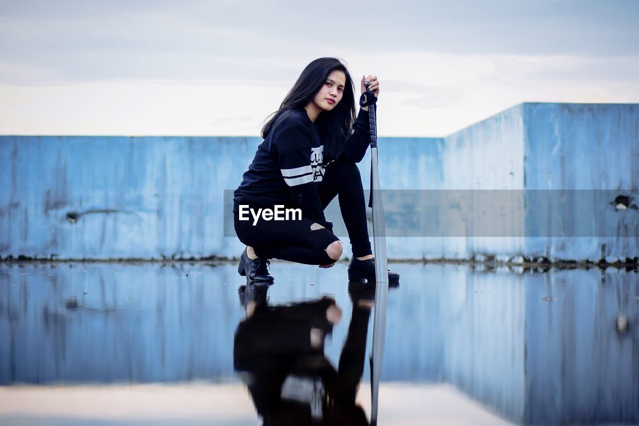 FULL LENGTH OF YOUNG WOMAN SITTING ON WATER