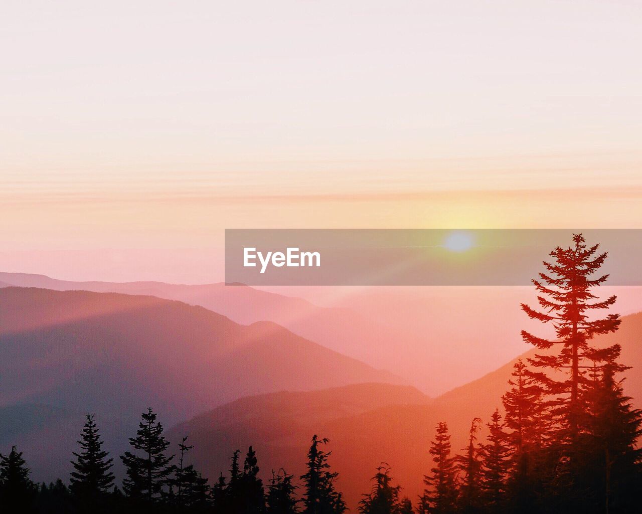 Scenic view of mountains with trees in foreground during sunset