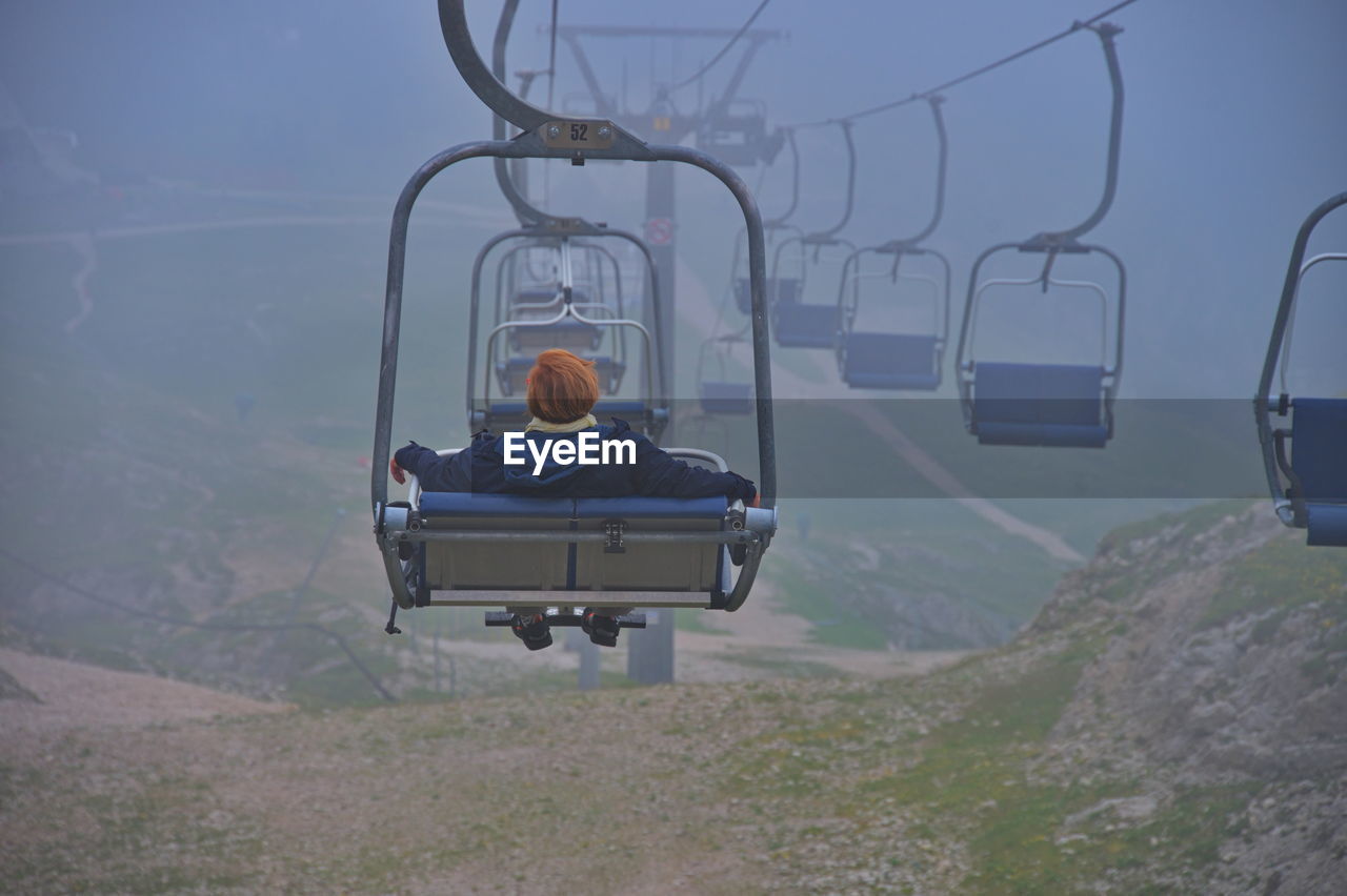 Senior woman sitting on cable car while riding over scenic landscape of italian dolomites
