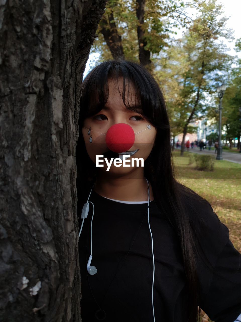 Woman with painted face looking away by tree trunk