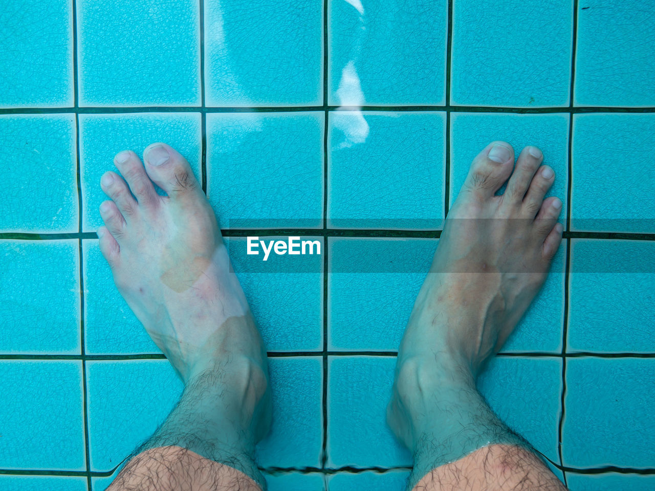 Low section of man standing on tiled floor in swimming pool