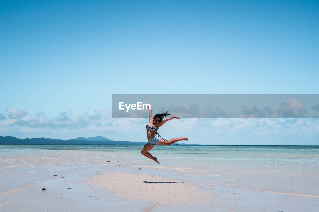 Young woman jumping at beach against blue sky