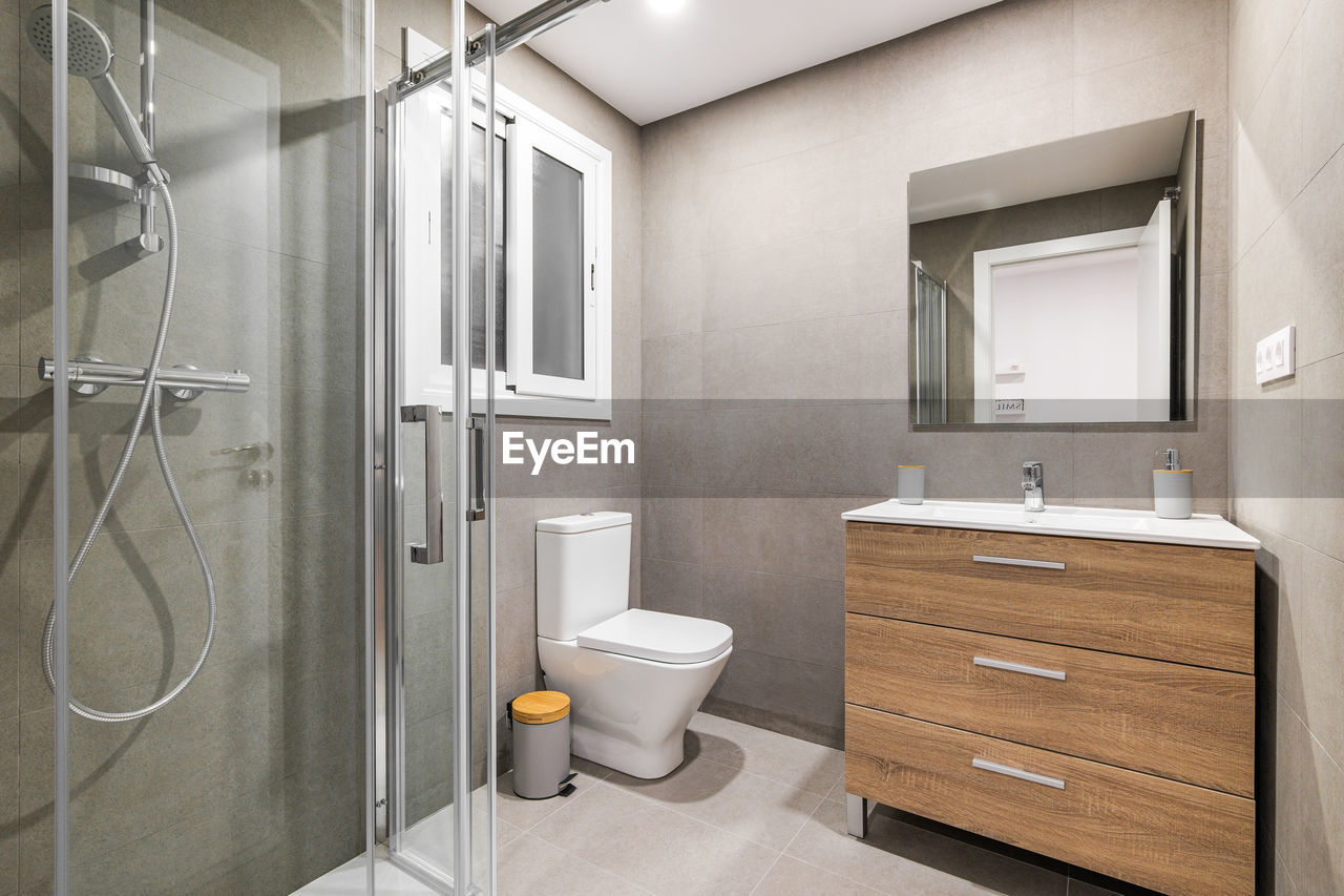 Modern refurbished bathroom with shower zone, toilet, wooden base with white sink and mirror.