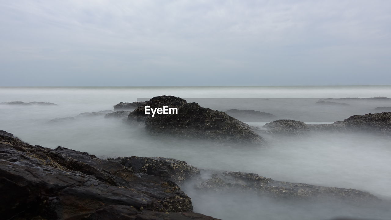 Rock formations by sea against sky in foggy weather