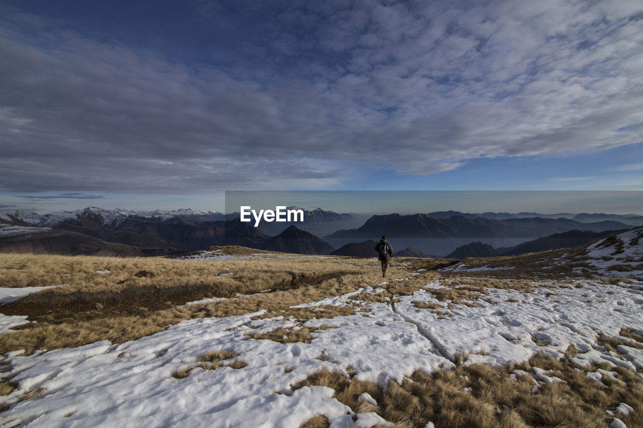 Rear view of hiker walking on snow covered field against sky