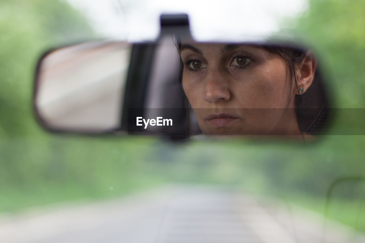Close-up of mature woman reflecting on rear-view mirror in car