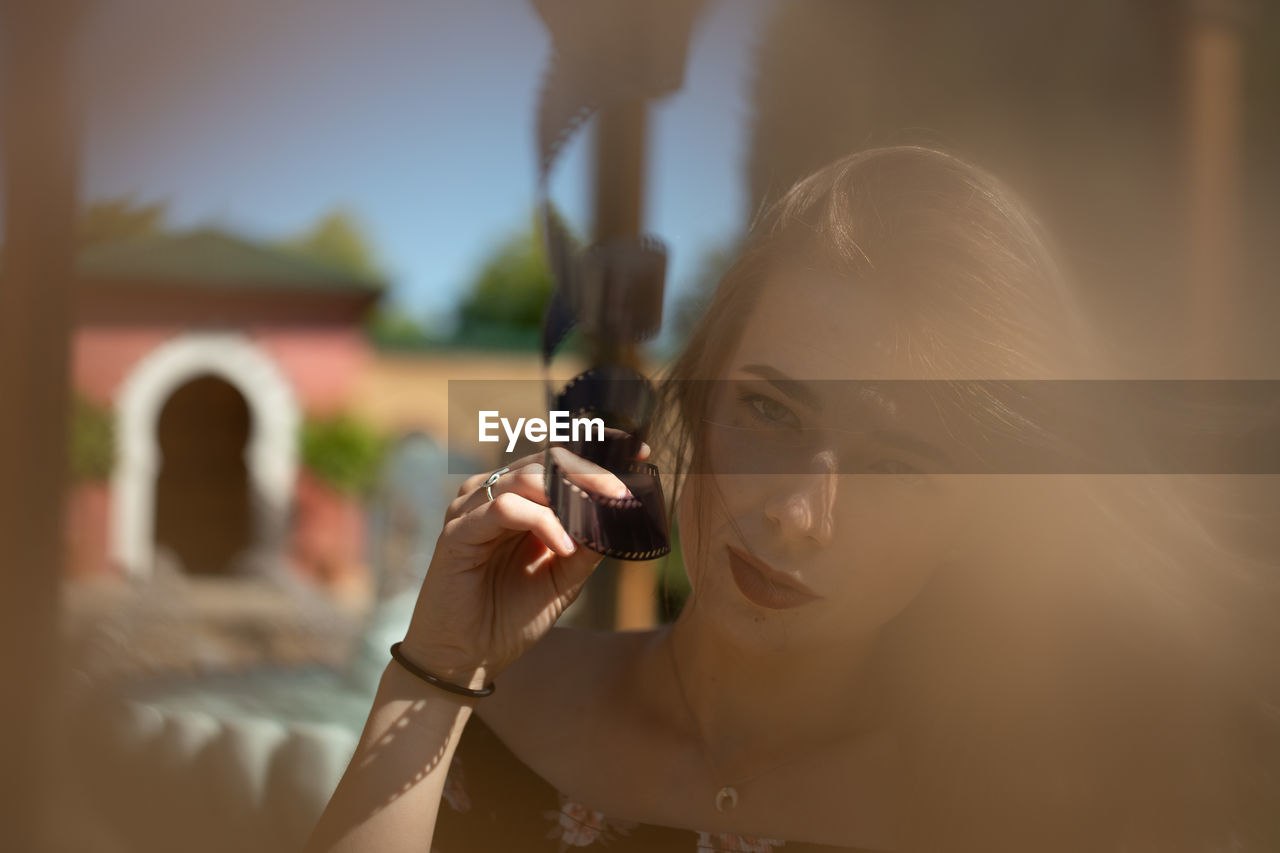 Portrait of woman holding film reel against sky