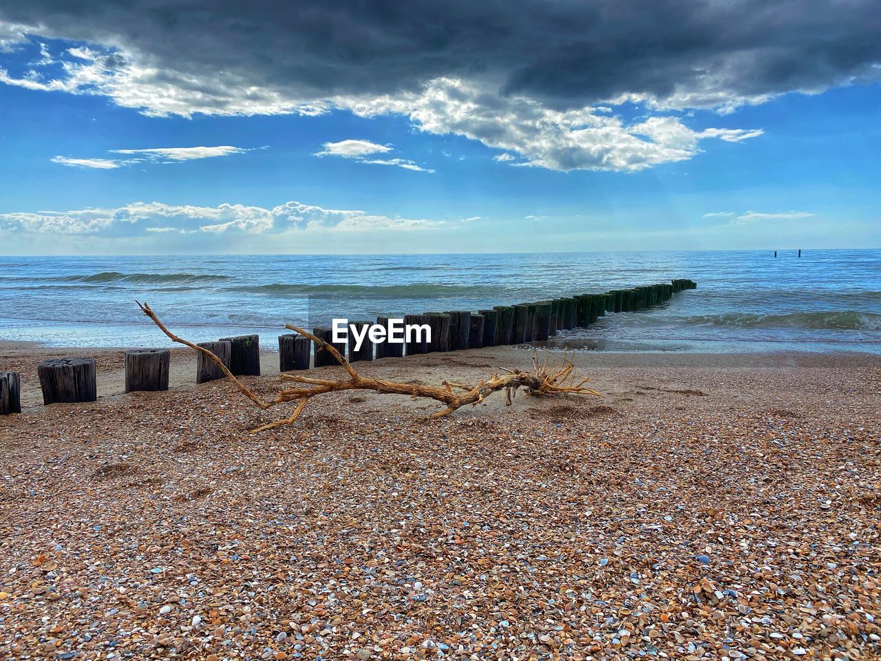 WOODEN POSTS ON BEACH BY SEA AGAINST SKY