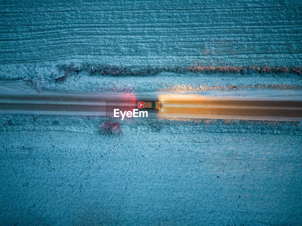Aerial view of a car driving through a forest at dusk in winter time. shot taken by a drone
