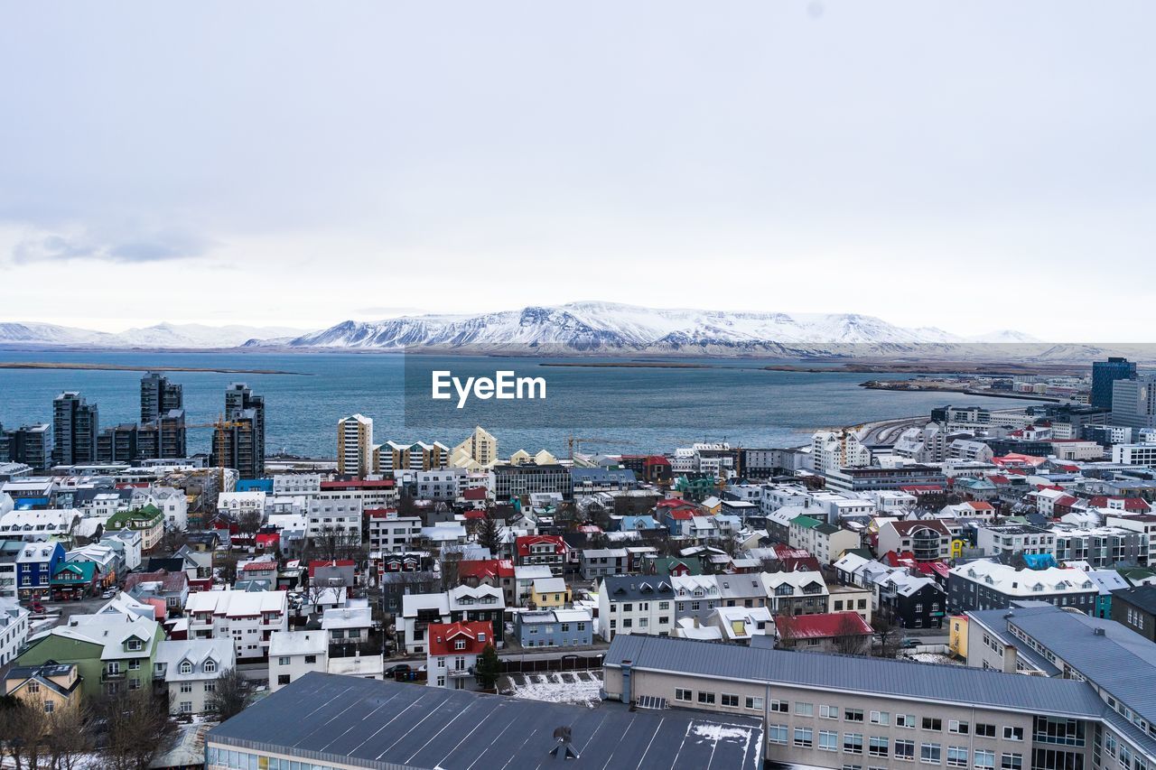 HIGH ANGLE VIEW OF BUILDINGS BY SEA AGAINST SKY IN CITY