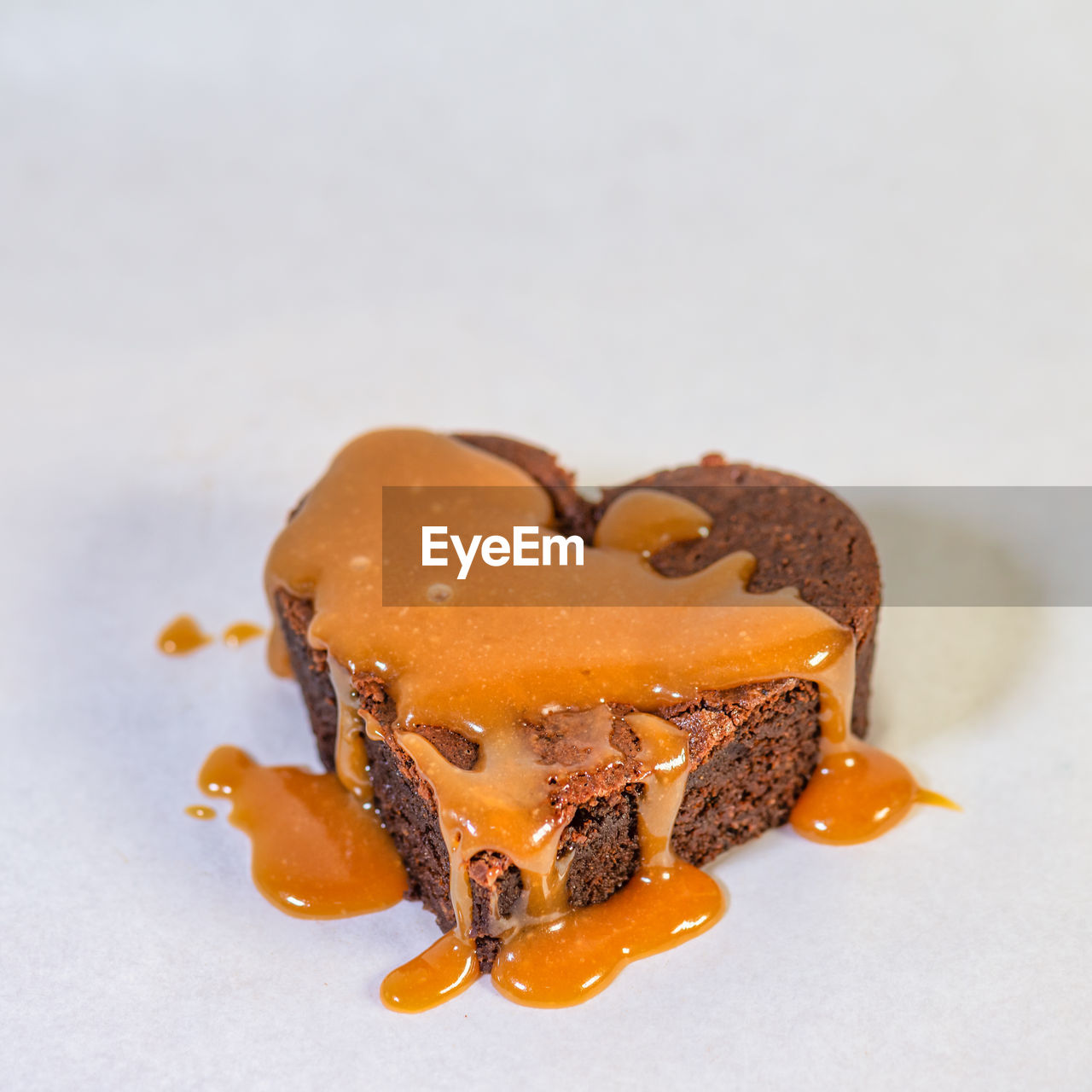 Heart shaped chocolate cake dripping with delicious caramel sauce, square photo