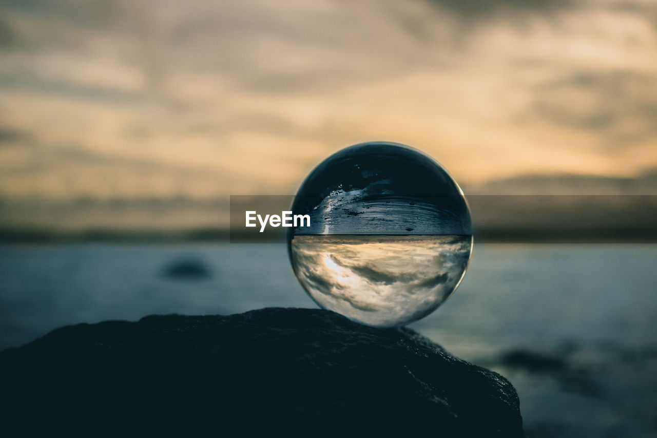 Close-up of crystal ball on rock against sky during sunset