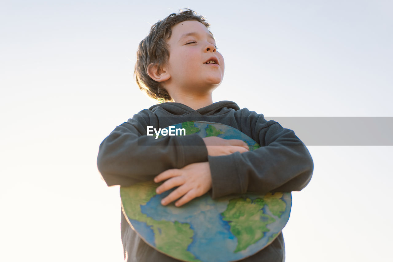 Boy embracing globe against sky