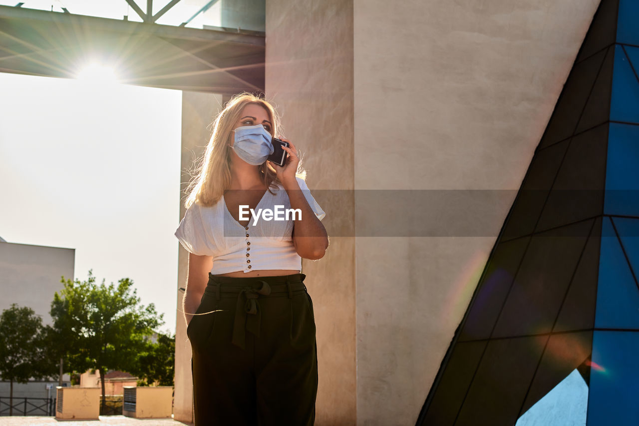 Young woman talks on the phone while wearing a mask