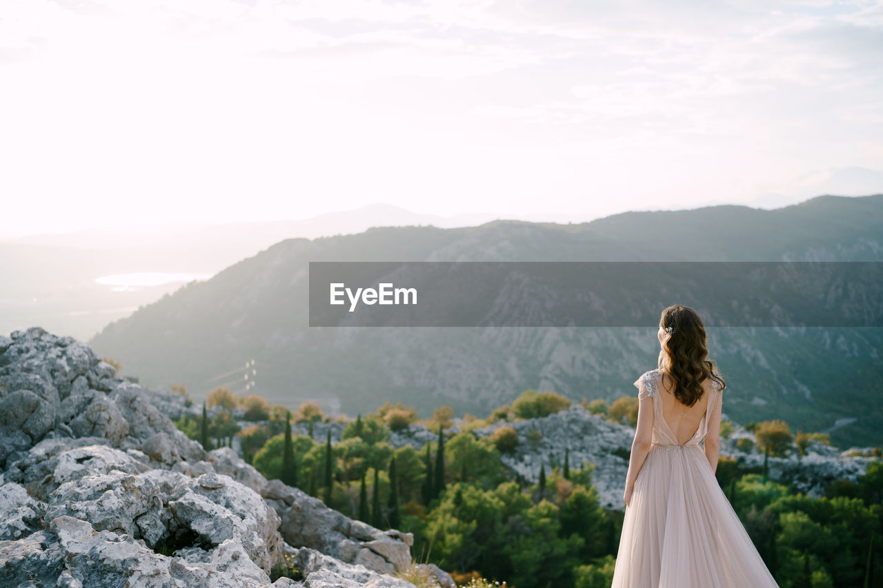 WOMAN STANDING BY MOUNTAIN AGAINST SKY