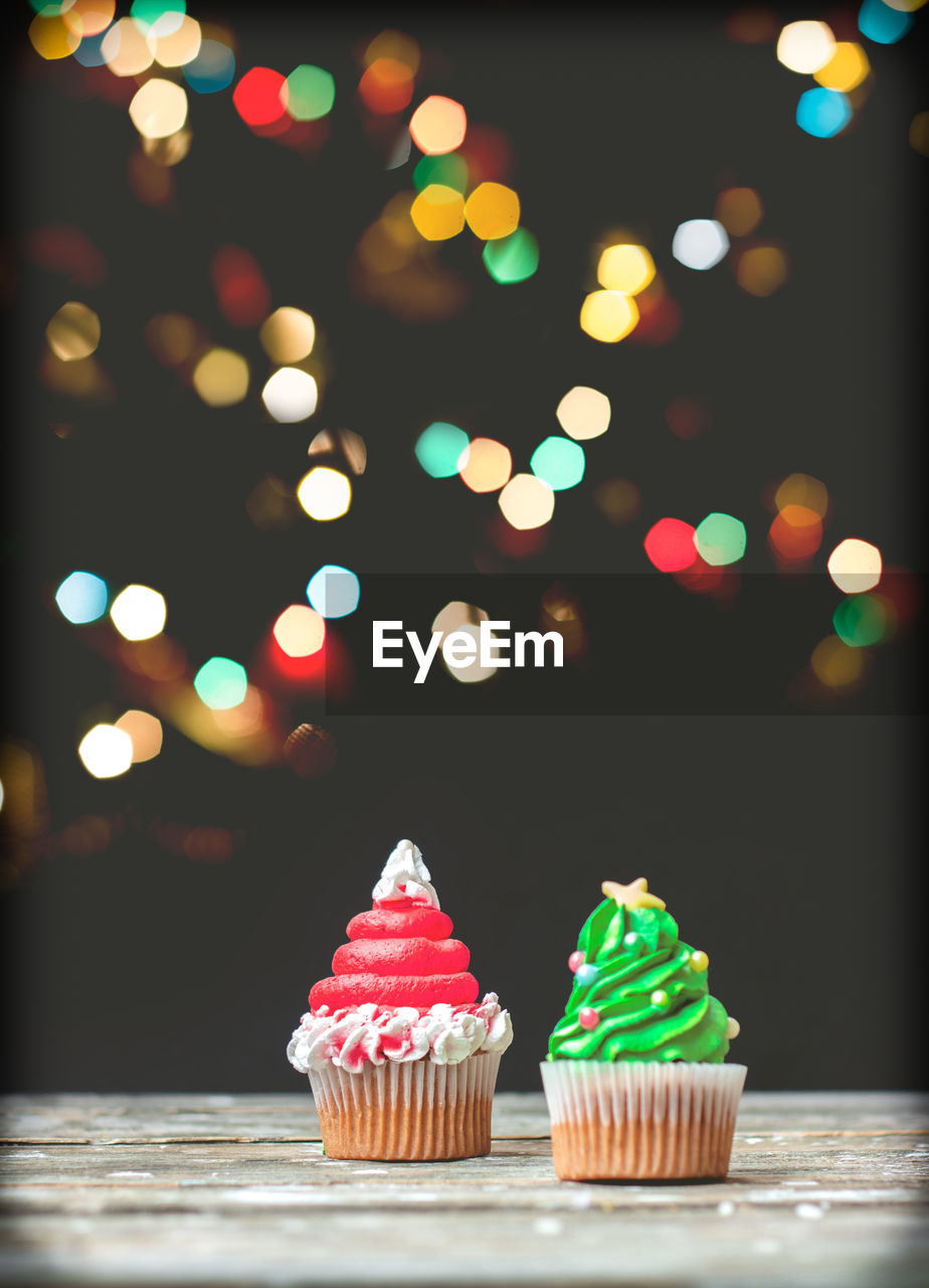 Vanilla cupcakes with christmas decoration, on dark background with colorful christmas lights