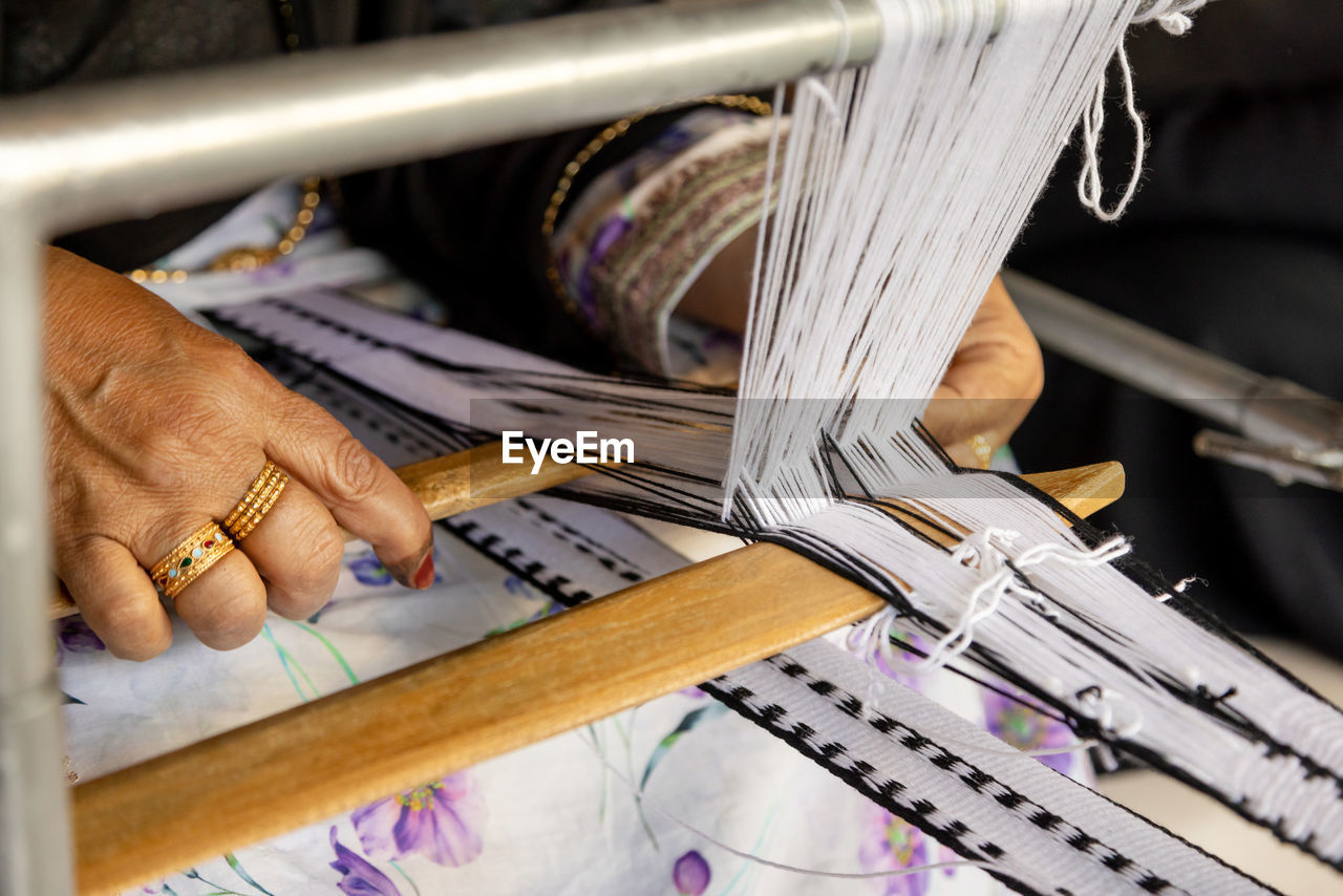 Closeup on hands of an old emirati woman using traditional weaving machine