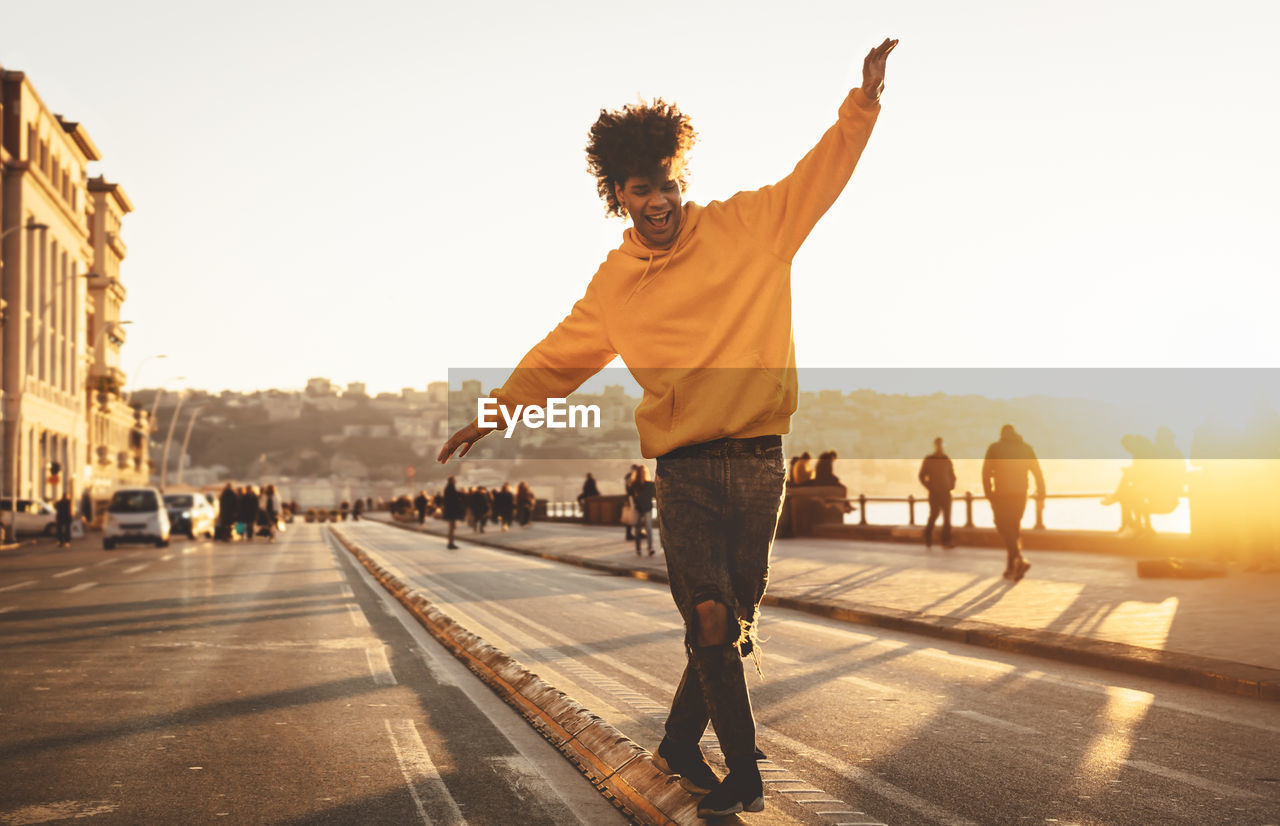 Full length of man walking on street in city against clear sky at sunset