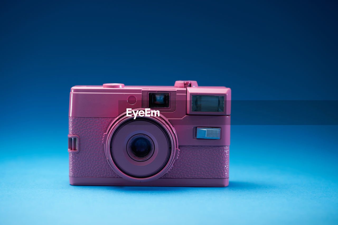 Pink color antique analog camera on blue background