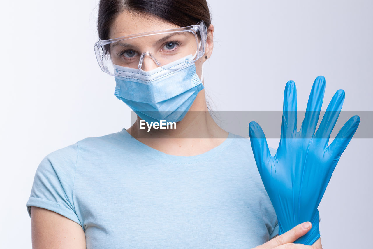 Portrait of doctor in mask wearing surgical glove against gray background