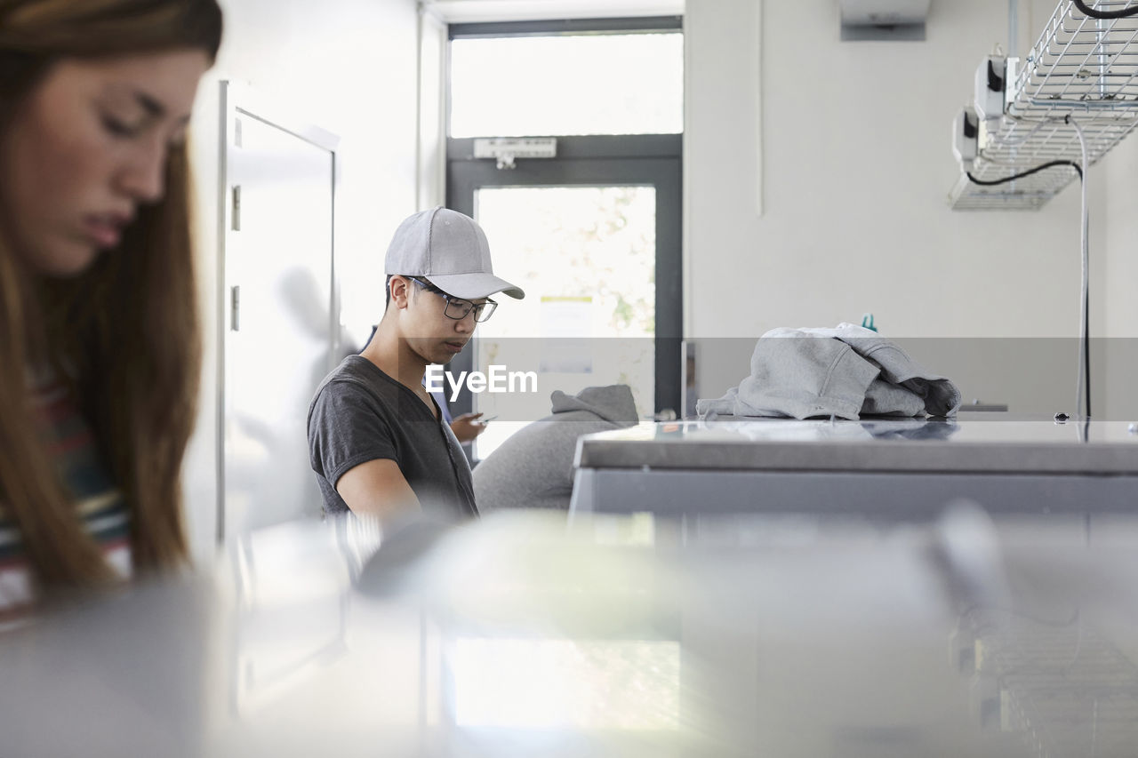 Young man with university friends doing laundry at laundromat